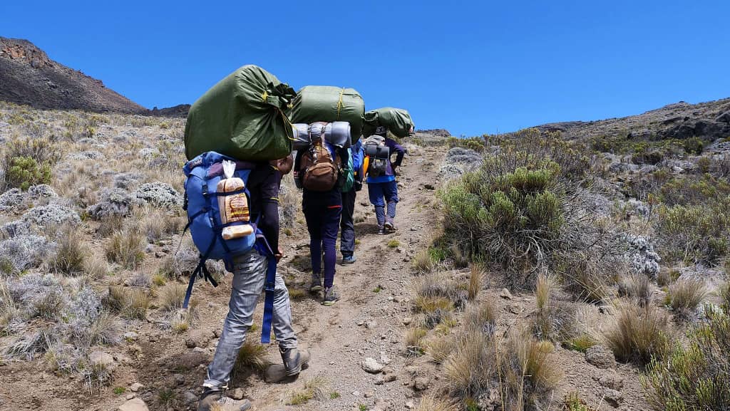 Porters carrying heavy loads up a steep dusty trail on Kilimanjaro