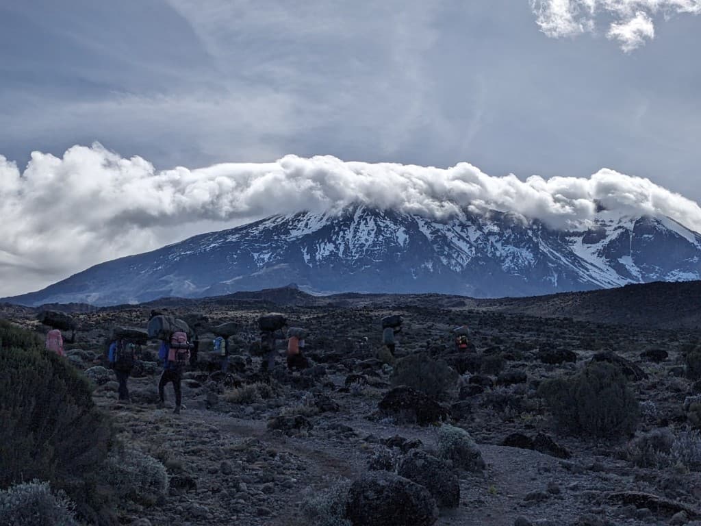 A line of porters walking toward Kilimanjaro with loads on their heads
