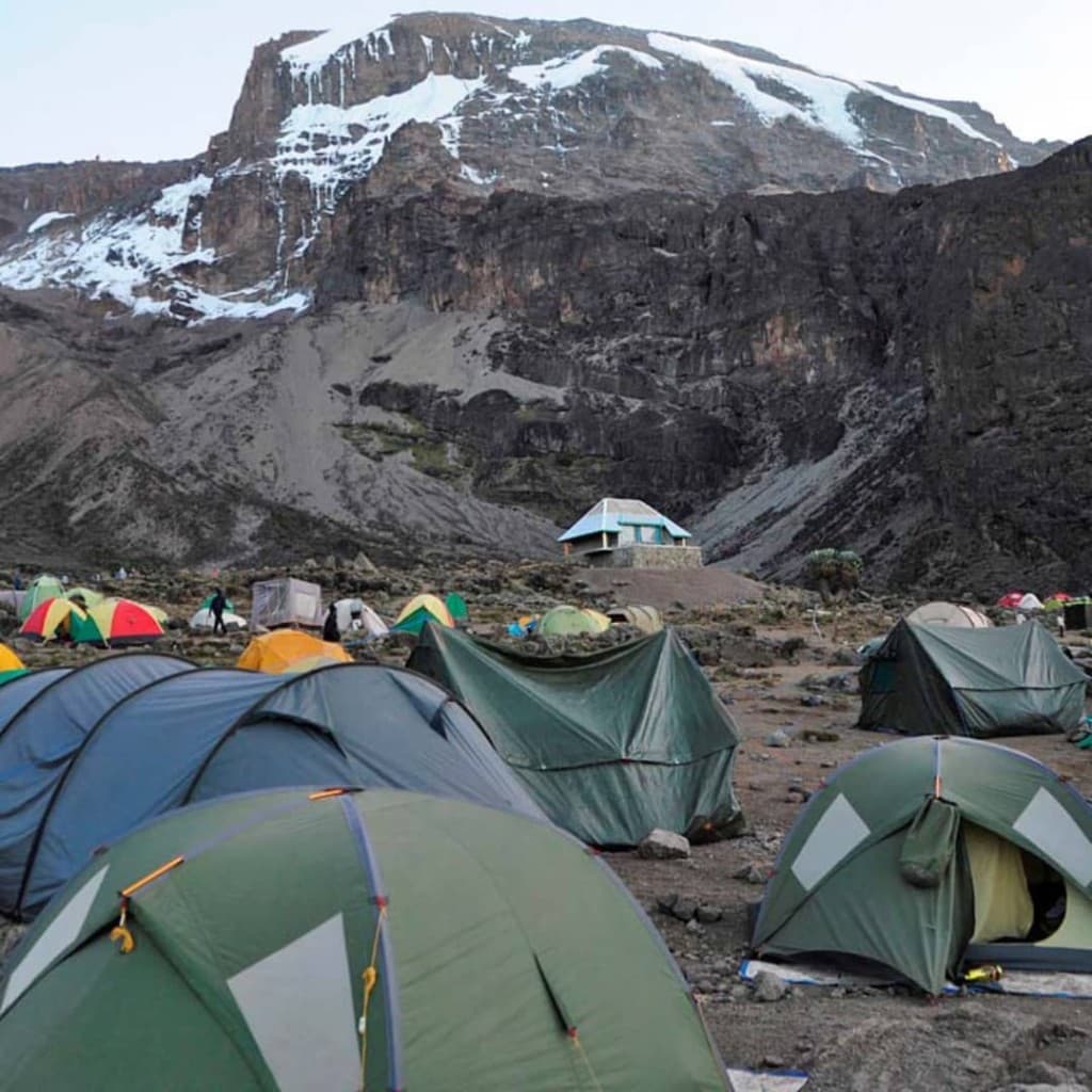 A high camp on Kilimanjaro with tents below a snow-streaked mountain wall