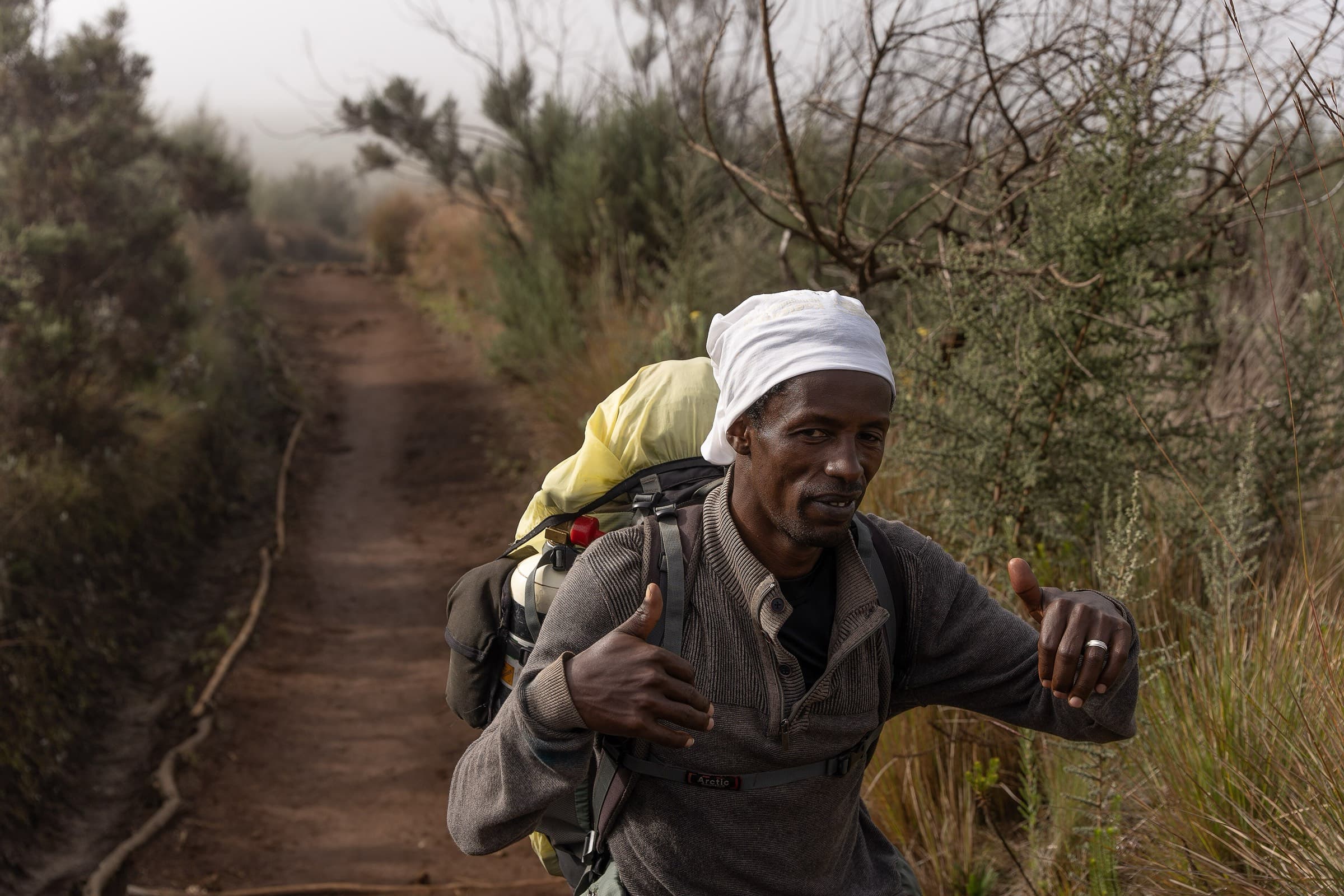 A Kilimanjaro mountain guide walking a forested trail with a pack