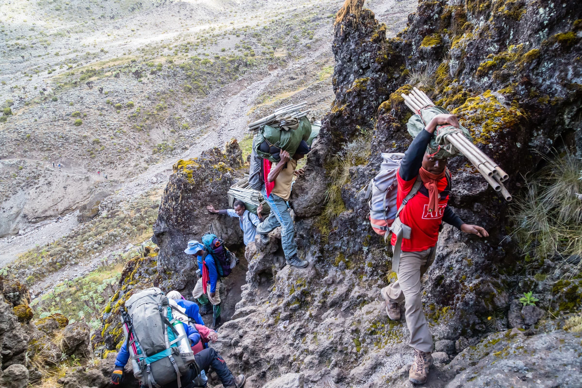 Porters carrying loads along a steep rocky traverse on Kilimanjaro